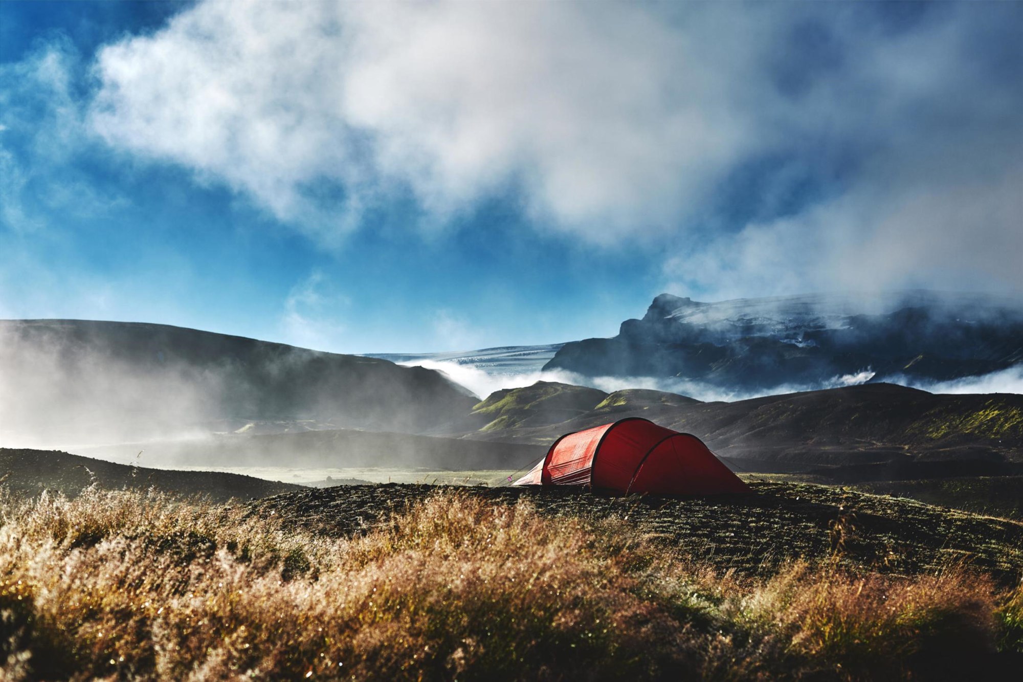 Wild Camping in the Icelandic Highlands A bright red tent pitched in the Icelandic highlands near Langisjór, surrounded by dramatic fog, mossy hills and distant glaciers – a breathtaking view of Iceland’s wild nature.