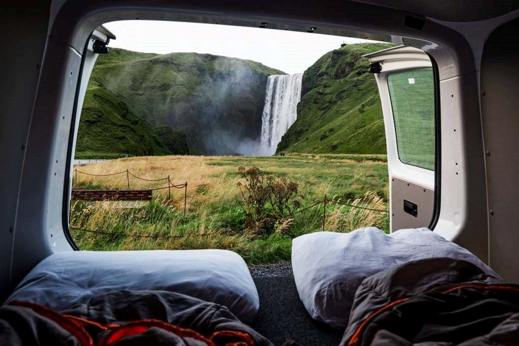 Campervan with a View of Skógafoss Waterfall The view from inside a campervan parked near Skógafoss waterfall in Iceland, with pillows and sleeping bags ready for a night next to one of the country’s most iconic spots.